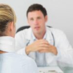 Male chiropractor talking to female patient wearing a neck brace while receiving comprehensive treatment after an accident