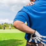 Man on the golf course holding his left shoulder blade and lower back for comfort