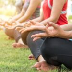 Four women sitting in a line on the grass doing meditative yoga