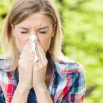 Young blonde woman blowing her nose in the park