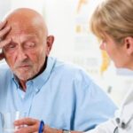 Older man holding head talking with doctor