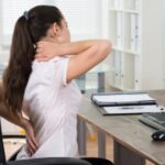 Young female office worker holding neck and back in pain