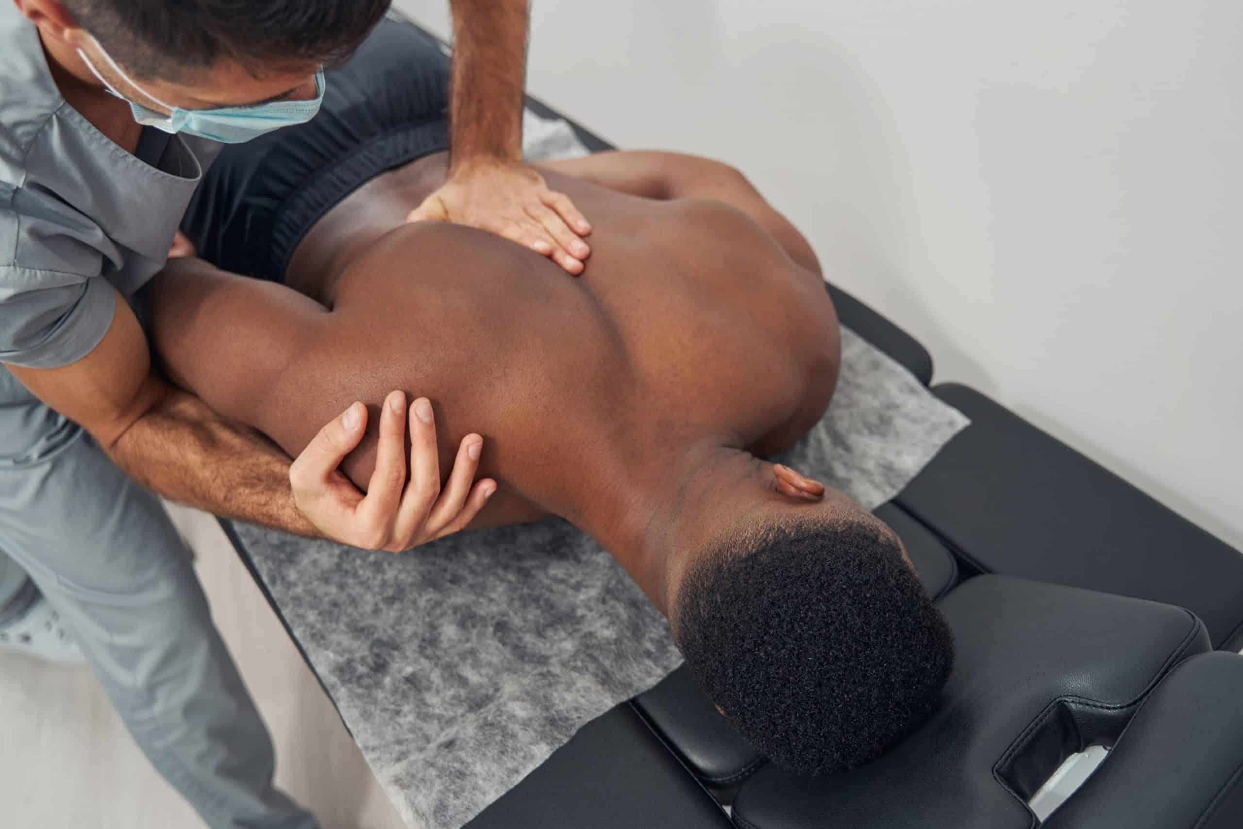 A man lying facedown on a table while a chiropractor does a spinal adjustment.