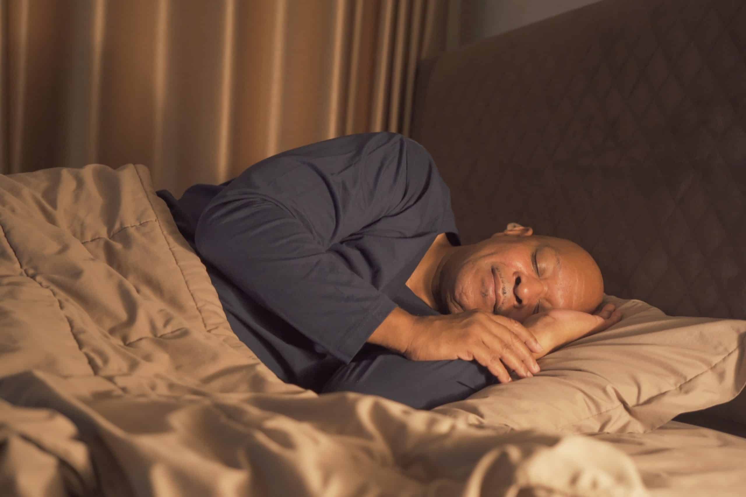 Male in pajamas sleeping restfully on his side in bed.