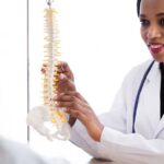 Female doctor in lab coat demonstrating an adjustment on a model spinal column.