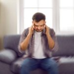 Man on sofa touching his temples to relieve the sense of vertigo.