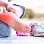 Person sitting on the ground holding an inflamed heel in their hands.