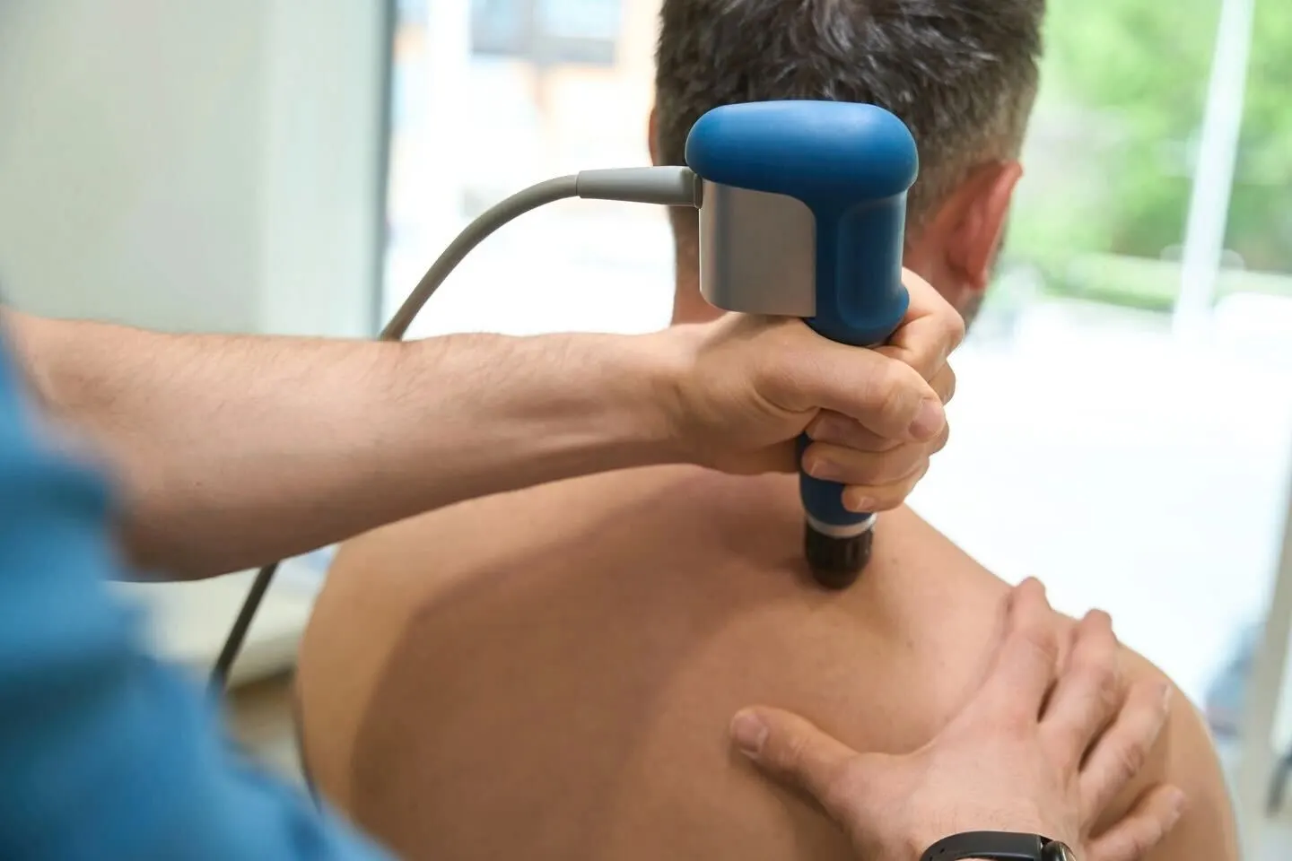 A chiropractor performing a back adjustment on a patient who is lying face down on a treatment table in a clinic. The chiropractor applies pressure with both hands to the patient's upper back.