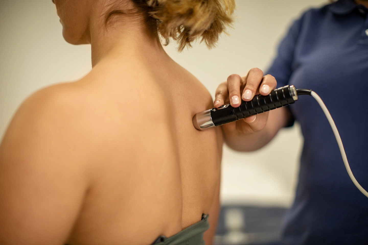 A chiropractor administering laser therapy treatment to a patient's lower back in a clinical setting. The patient is comfortably lying on a treatment table while the chiropractor directs the therapeutic laser device towards the targeted area, highlighting advanced treatment options in chiropractic care