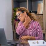 Woman at a desk holding her neck.