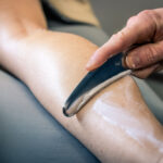 A muscle-scraping tool being guided across the calf.