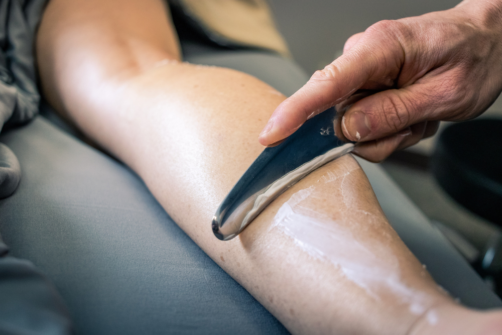 A muscle-scraping tool being guided across the calf.