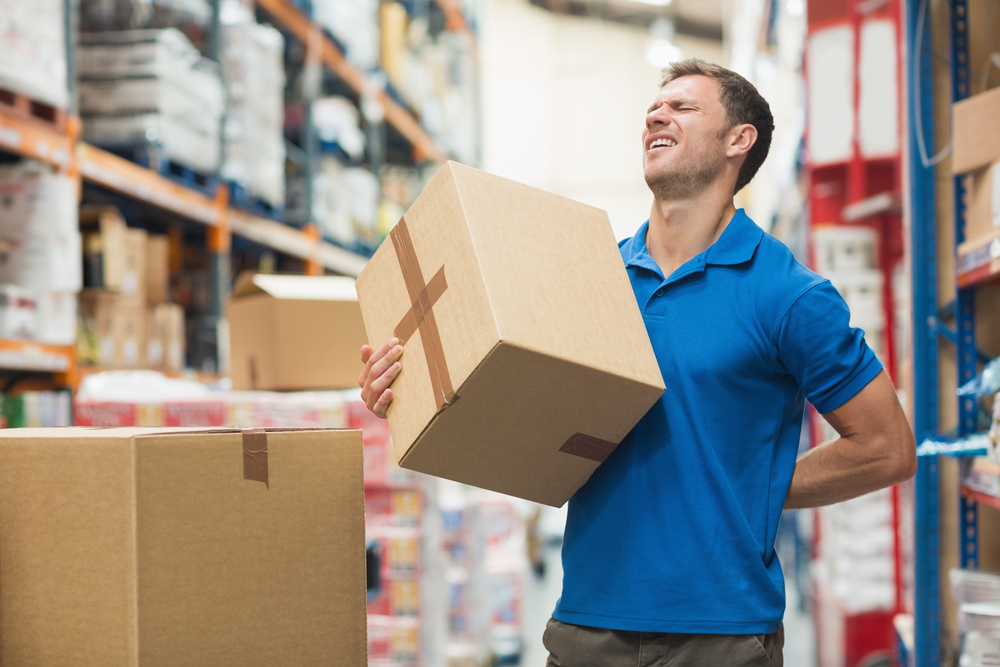 Man lifting a box with one hand and holding his back with the other.