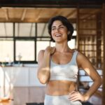 Smiling woman in athletic wear standing confidently in a sunlit wellness studio, representing the positive effects of holistic chiropractic care and a healthy lifestyle.