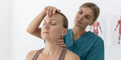 A healthcare specialist in blue scrubs performs a gentle manual neck adjustment on a female patient to relieve chronic headache pain in a Fort Lauderdale clinic.