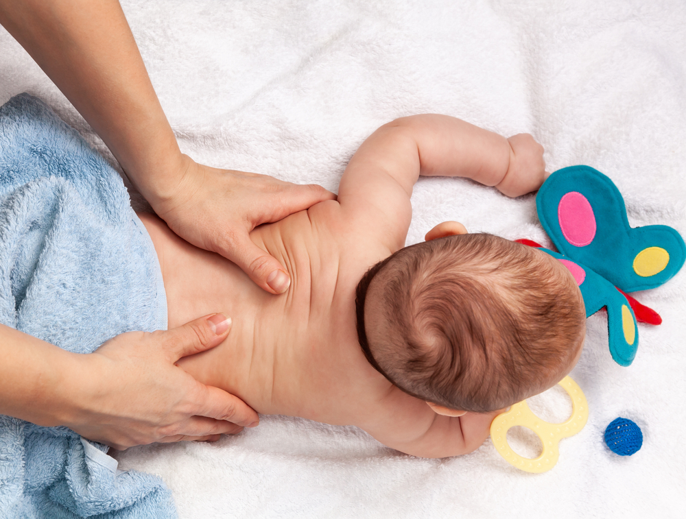 A healthcare specialist uses gentle hand pressure to perform a wellness adjustment on an infant lying on a soft white towel in an Aventura clinic.