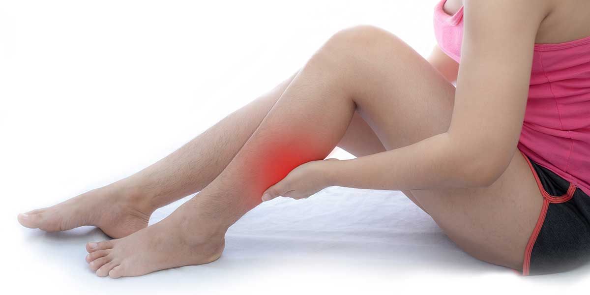 A person holding their calf muscle in discomfort, demonstrating what causes burning leg pain with sciatica along the nerve.