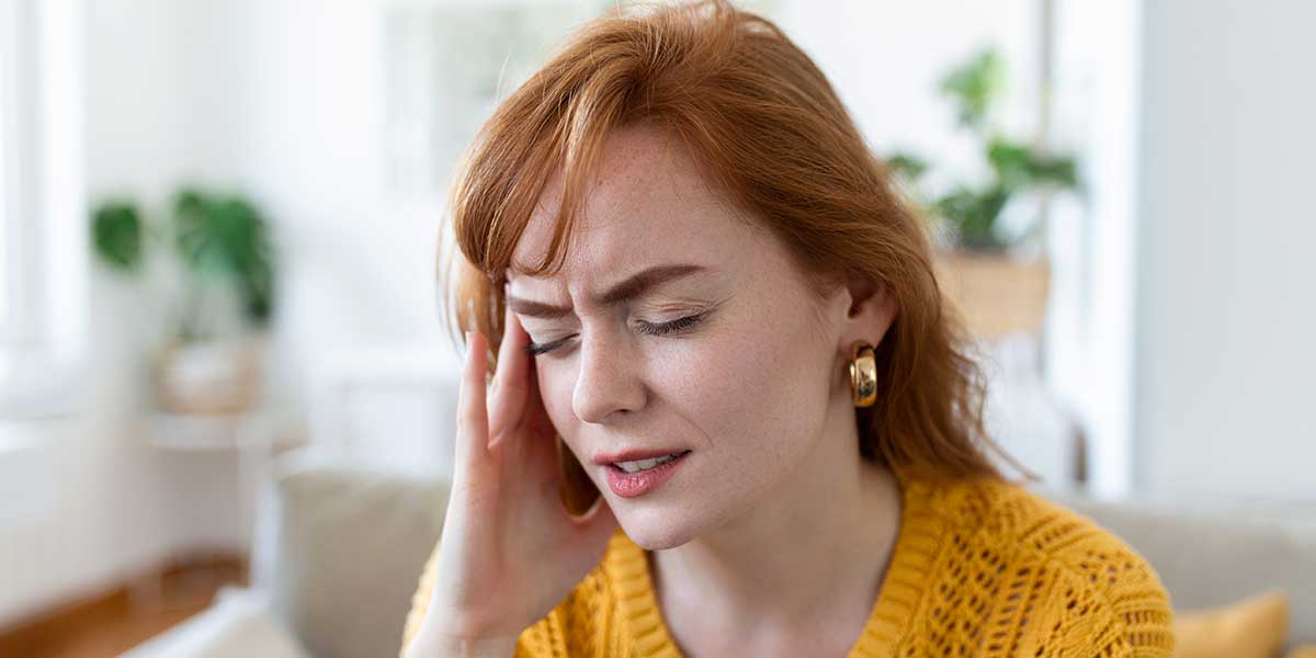 A woman wincing and holding her temple in discomfort, highlighting a discussion on identifying common migraine triggers and symptoms.
