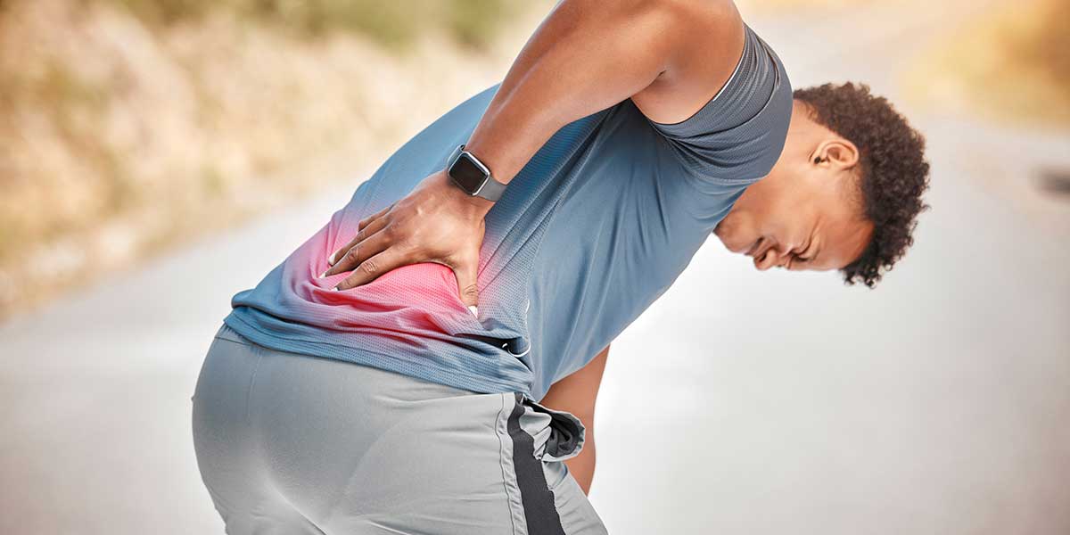 A man outdoors gripping his lower back in pain, highlighting why your lower back hurts after a leg day workout.