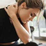 A woman in a gym holding her neck in discomfort, illustrating why your neck hurts after lifting weights incorrectly.