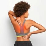 A woman touching her back in discomfort, illustrating what causes upper back pain between your shoulder blades after exercising.