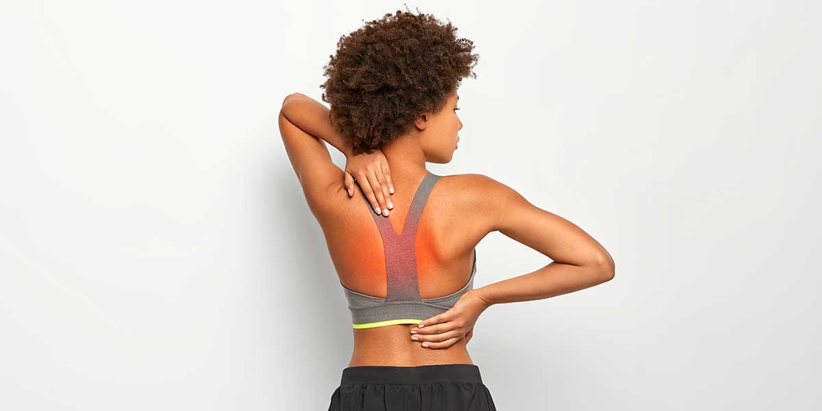 A woman touching her back in discomfort, illustrating what causes upper back pain between your shoulder blades after exercising.