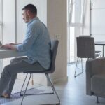 A man sitting at a desk using his laptop, understanding how a sedentary lifestyle affects posture and joint mobility.