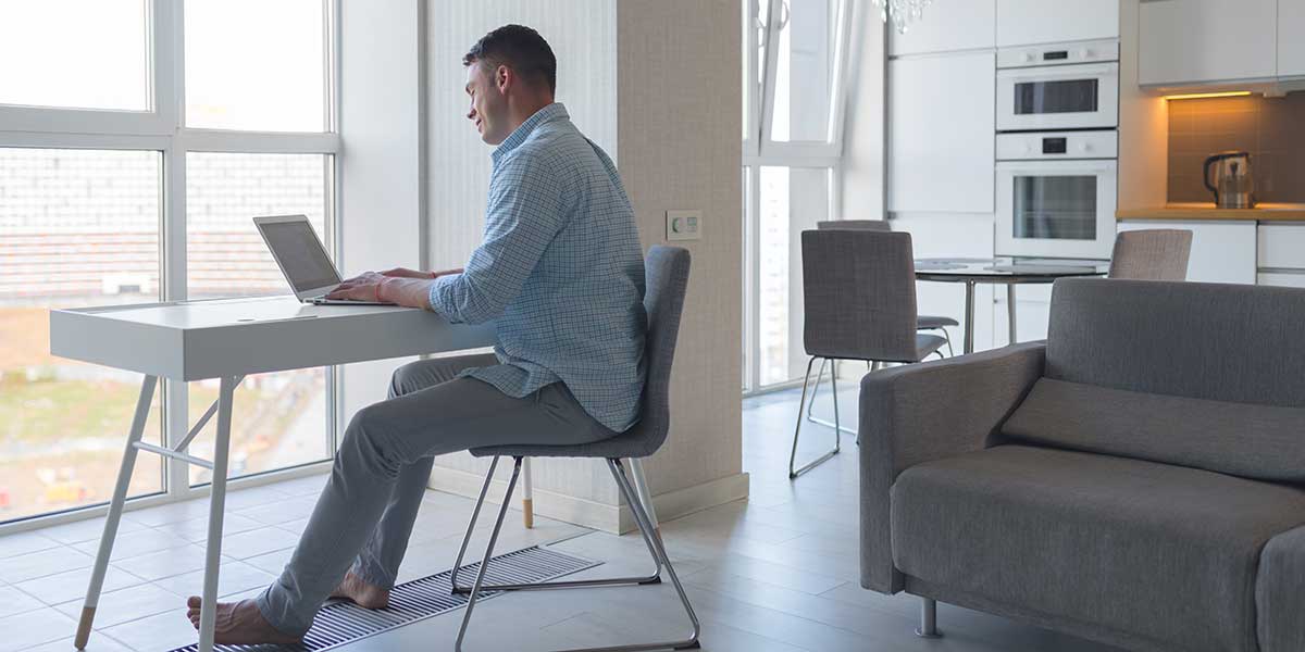 A man sitting at a desk using his laptop, understanding how a sedentary lifestyle affects posture and joint mobility.
