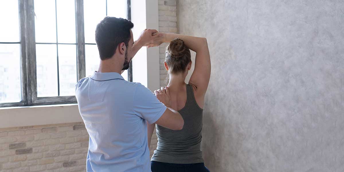 A physical therapist guides a woman through an upper body stretch, highlighting professional postural restoration therapy in Weston, FL.