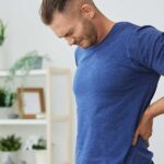 A man wincing in pain while holding his lower back, demonstrating how weak core muscles can cause severe back pain.