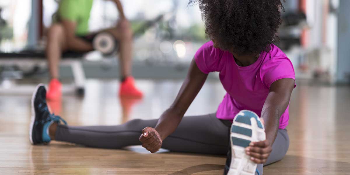 Woman stretching her legs on a gym floor, demonstrating the critical importance of warming up properly before a workout.