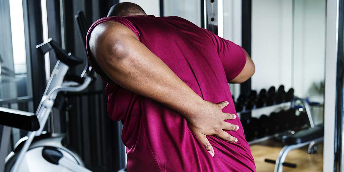 Man at the gym holding his lower back in pain, showcasing everyday habits that can aggravate a herniated disc.