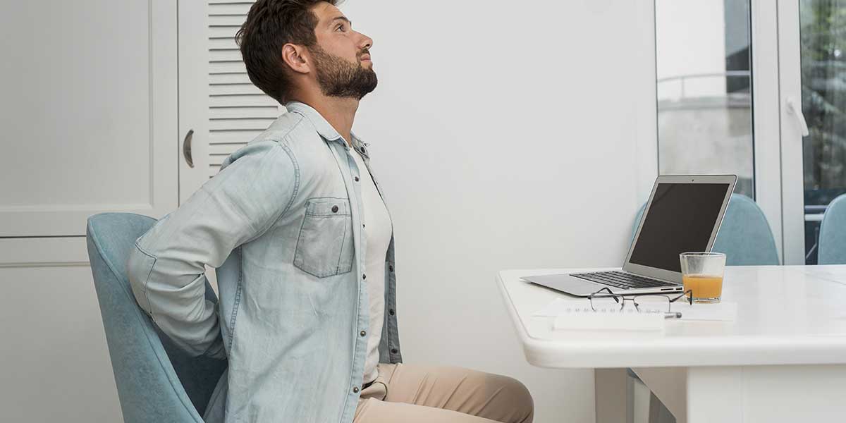 Man holding his lower back while sitting at a desk, illustrating poor posture and daily habits that trigger sciatica pain.