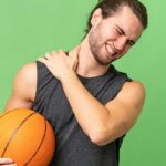 Basketball player clutching his sore shoulder in pain, demonstrating common upper extremity sports injuries caused by throwing and overhead motions.