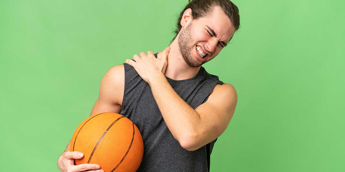 Basketball player clutching his sore shoulder in pain, demonstrating common upper extremity sports injuries caused by throwing and overhead motions.