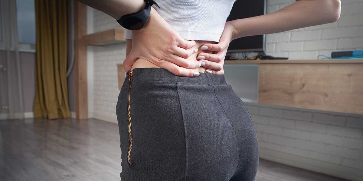 Person holding lower back, representing pain centralization near the spine, which is one key sign sciatica is improving.