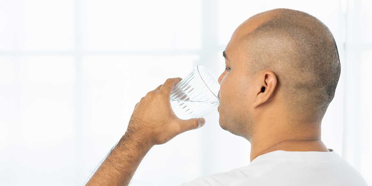 Man drinking a glass of fresh water, illustrating why proper hydration is essential following professional chiropractic spinal adjustments.