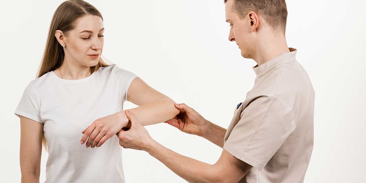 Physical therapist examining and supporting a woman's elbow joint during an elbow pain assessment in Port St Lucie, FL.