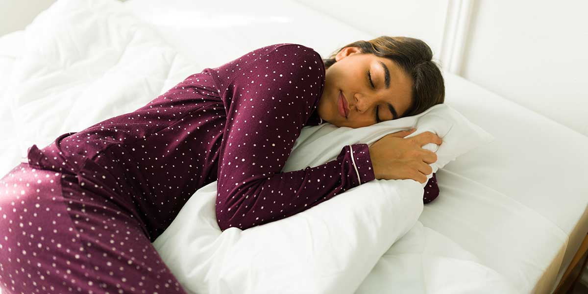 Woman sleeping on her side hugging a pillow, illustrating how improper sleeping positions and posture cause neck pain.