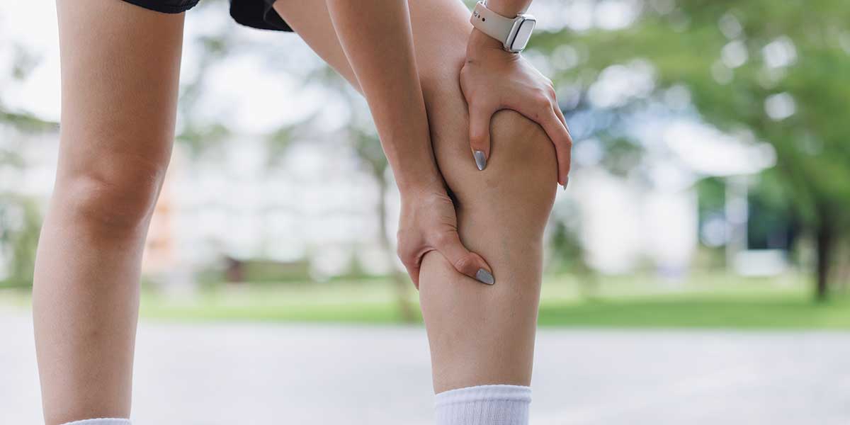Runner gripping her lower leg in distress, showcasing sharp, electric pain shooting down the calf muscle during outdoor exercise.