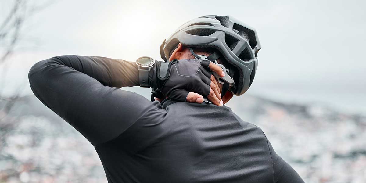 Cyclist wearing a helmet holding the back of his neck in discomfort, highlighting neck pain caused by bike riding.